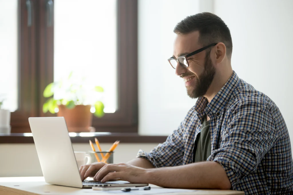 Homem sentado em frente ao notebook em sua mesa, digitando.