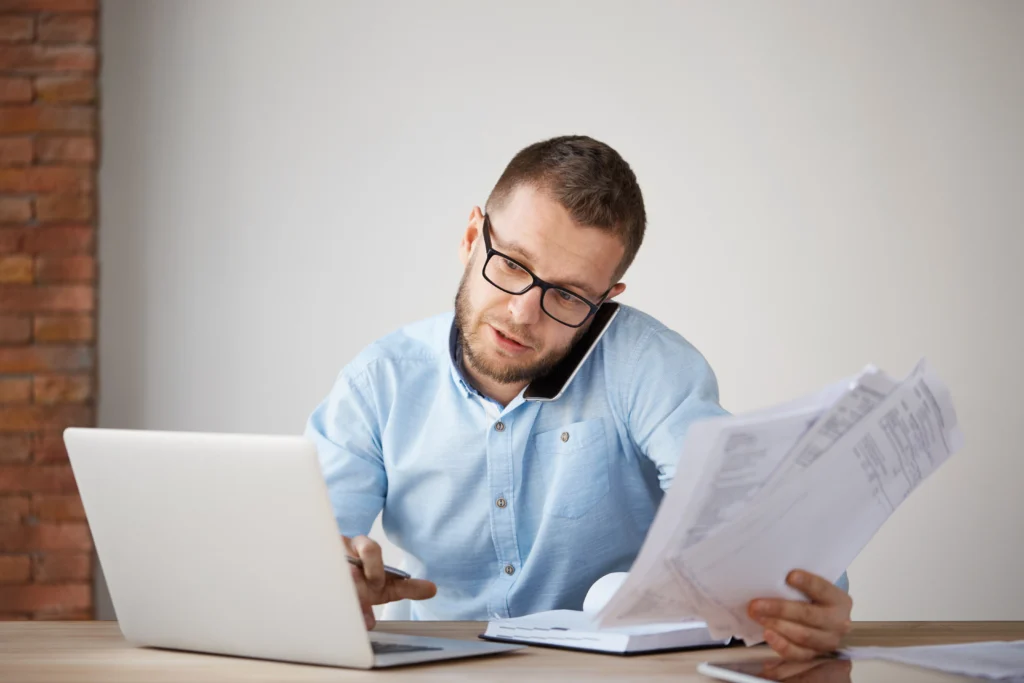 Homem em escritório sentado à mesa com papelada e notebook representando a busca automática por nota fiscal de serviço eletrônica.