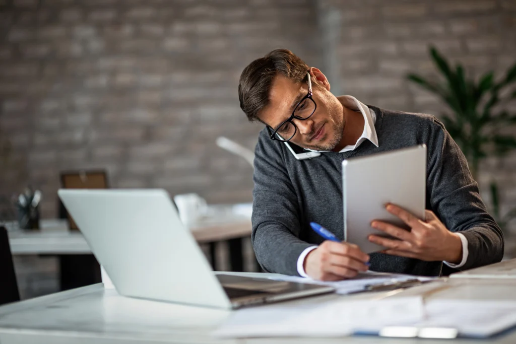 Homem trabalhando com notebook aberto e tablet na mão, representando pesquisa na tabela ncm.